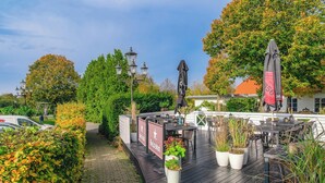 An outdoor patio area with tables and chairs, potted plants, and a sign for Heineken. - Hotel Årslev Kro (Aarhus)