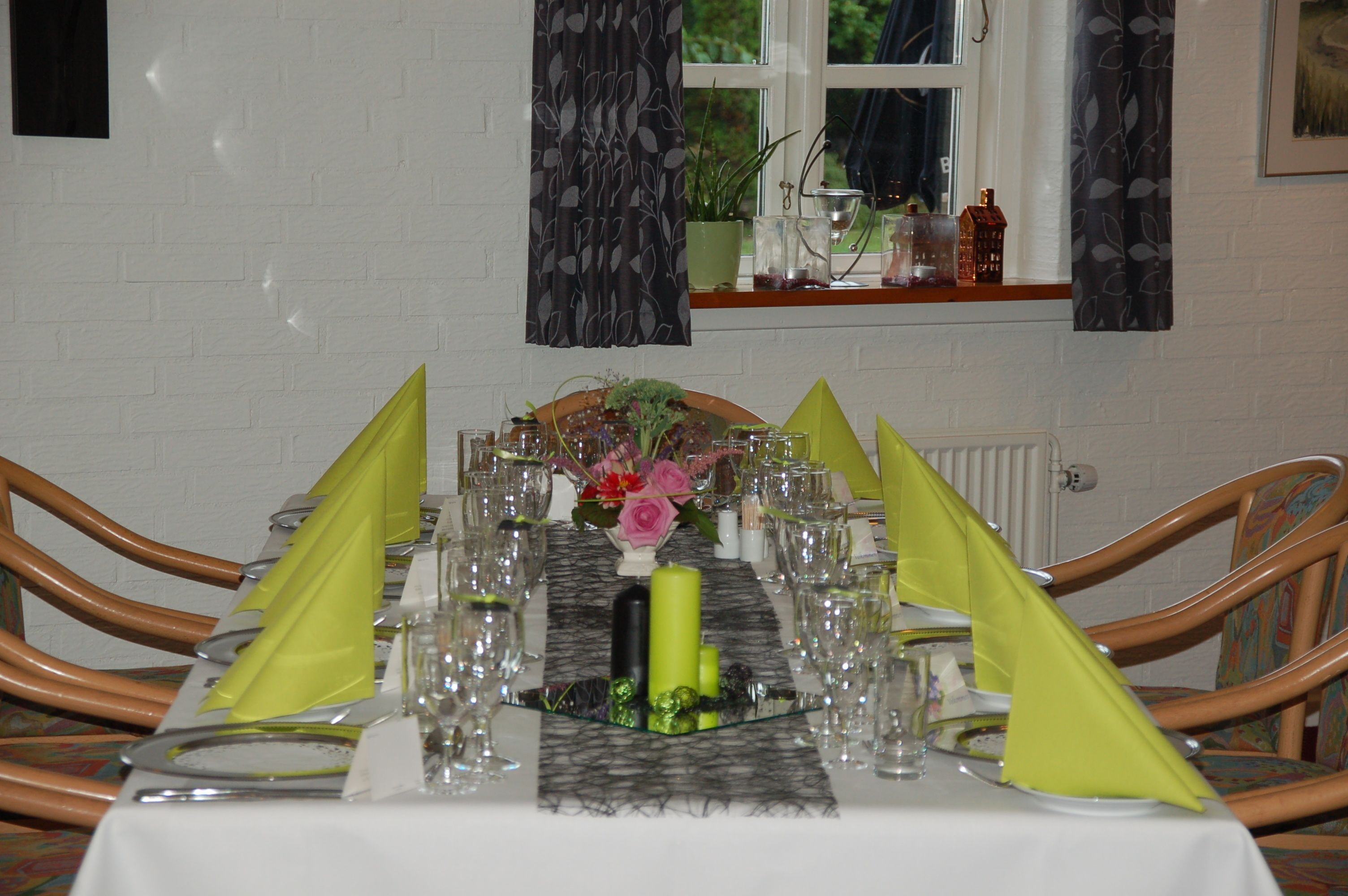 A dining table set for a meal with chairs, a window with curtains, and a small plant on the windowsill.