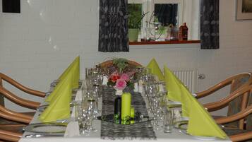 A dining table set for a meal with chairs, a window with curtains, and a small plant on the windowsill.