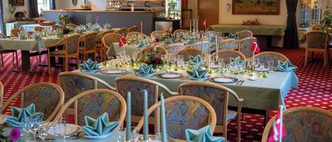 A dining area with tables set for a meal, chairs, and a bar in the background.