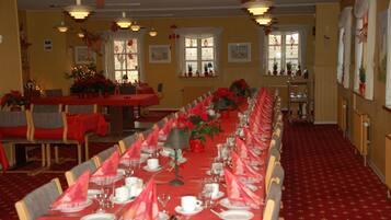 A dining hall with long tables set for a meal, decorated with red napkins and floral centerpieces.