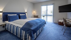 A hotel room with a large bed, a desk, a chair, a TV, and a balcony with a view. - Strandhotellet (Ebeltoft)