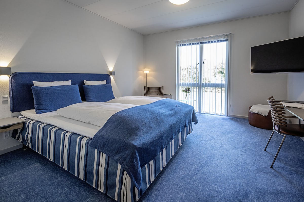 Een hotelkamer met een groot bed, een bureau, een stoel, een televisie en een balkon met uitzicht.