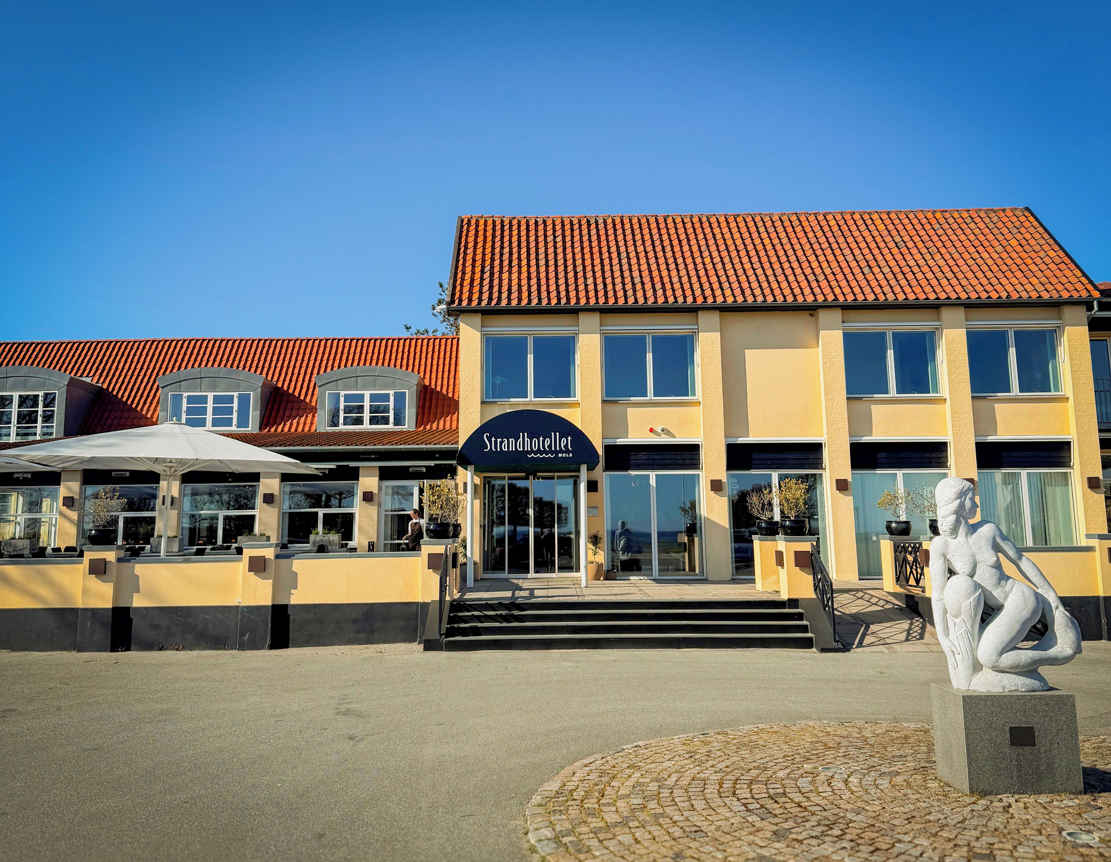 Ein Hotel mit Ziegeldach, einem zentralen Eingang und einer Statue im Vordergrund.