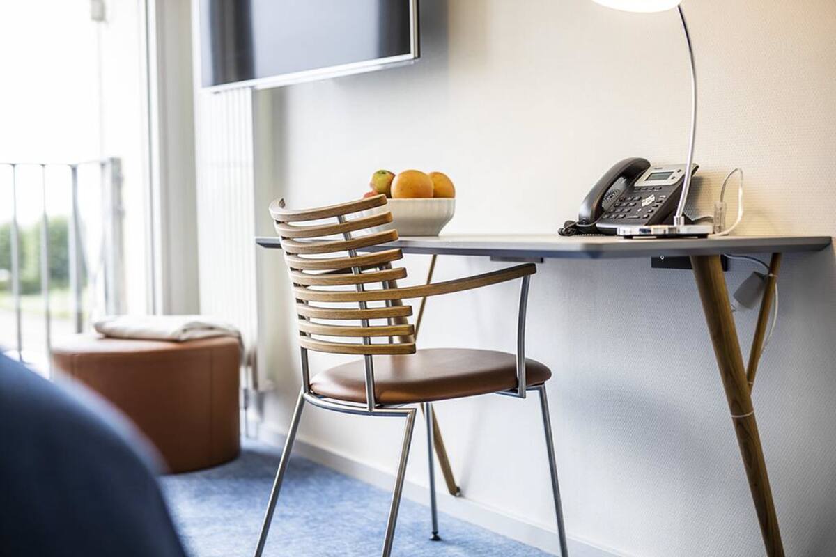 Een moderne hotelkamer met een houten stoel, een klein tafeltje met een fruitschaal, een telefoon en een aan de muur bevestigde televisie.