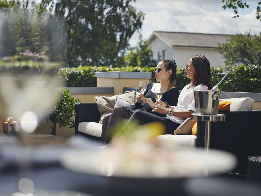 A couple sitting on a sofa with a glass of wine, a bottle, and a small table with a bowl and a plant.