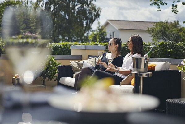 A couple sitting on a sofa with a glass of wine, a bottle, and a small table with a bowl and a plant. - Strandhotellet (Ebeltoft)