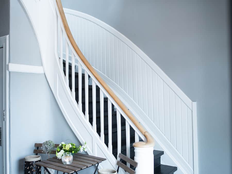 A staircase with white railings and a wooden handrail, leading to a landing with a small table and chairs.