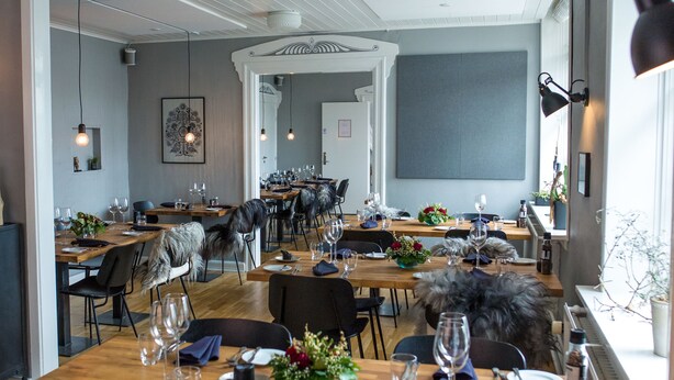 A modern dining area with wooden tables and black chairs, featuring a large window with a view of the outdoors. - Refborg Hotel & Spiseri (Billund)