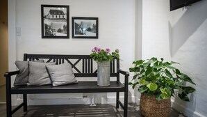 A black bench with cushions, a metal vase with flowers, and a large potted plant against a white wall with two framed pictures. - Refborg Hotel & Spiseri (Billund)