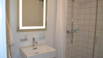 Un baño con lavamanos blanco, un espejo y una zona de ducha con paredes de azulejos.