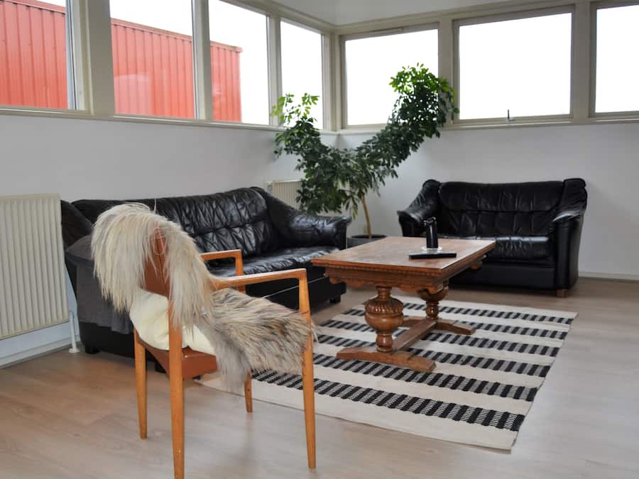 Uma sala de estar com um sofá de couro preto, uma cadeira de madeira com um cobertor de pele, uma mesa de centro de madeira e um tapete listrado.