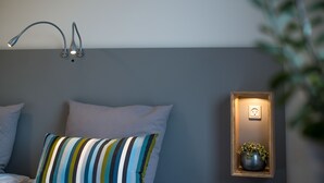 A bedroom with a bed, striped pillow, wall-mounted lamp, and a small shelf with a plant. - Refborg Hotel & Spiseri (Billund)