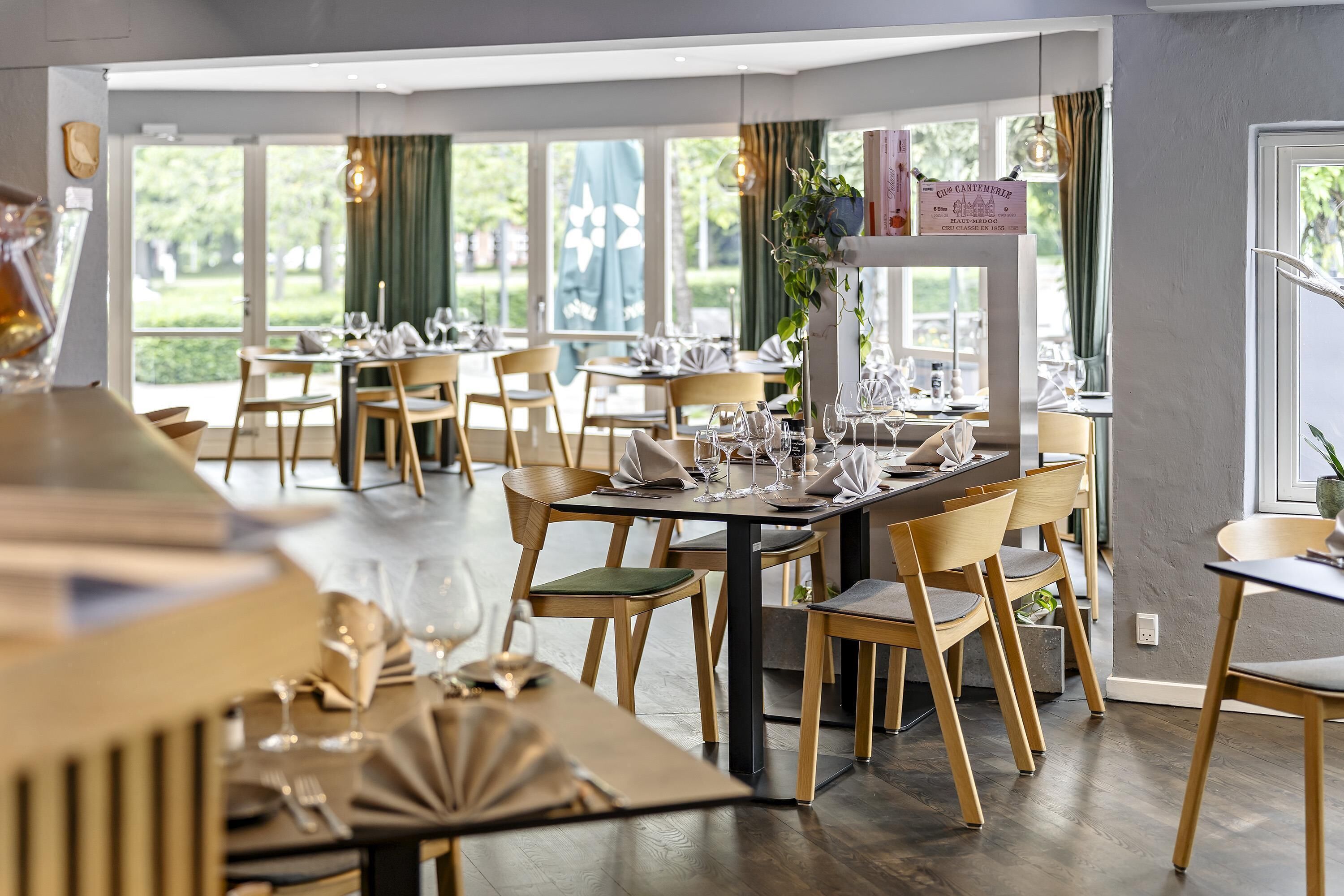 Un restaurante con varias mesas dispuestas para comer, sillas de madera y vistas a zonas verdes.
