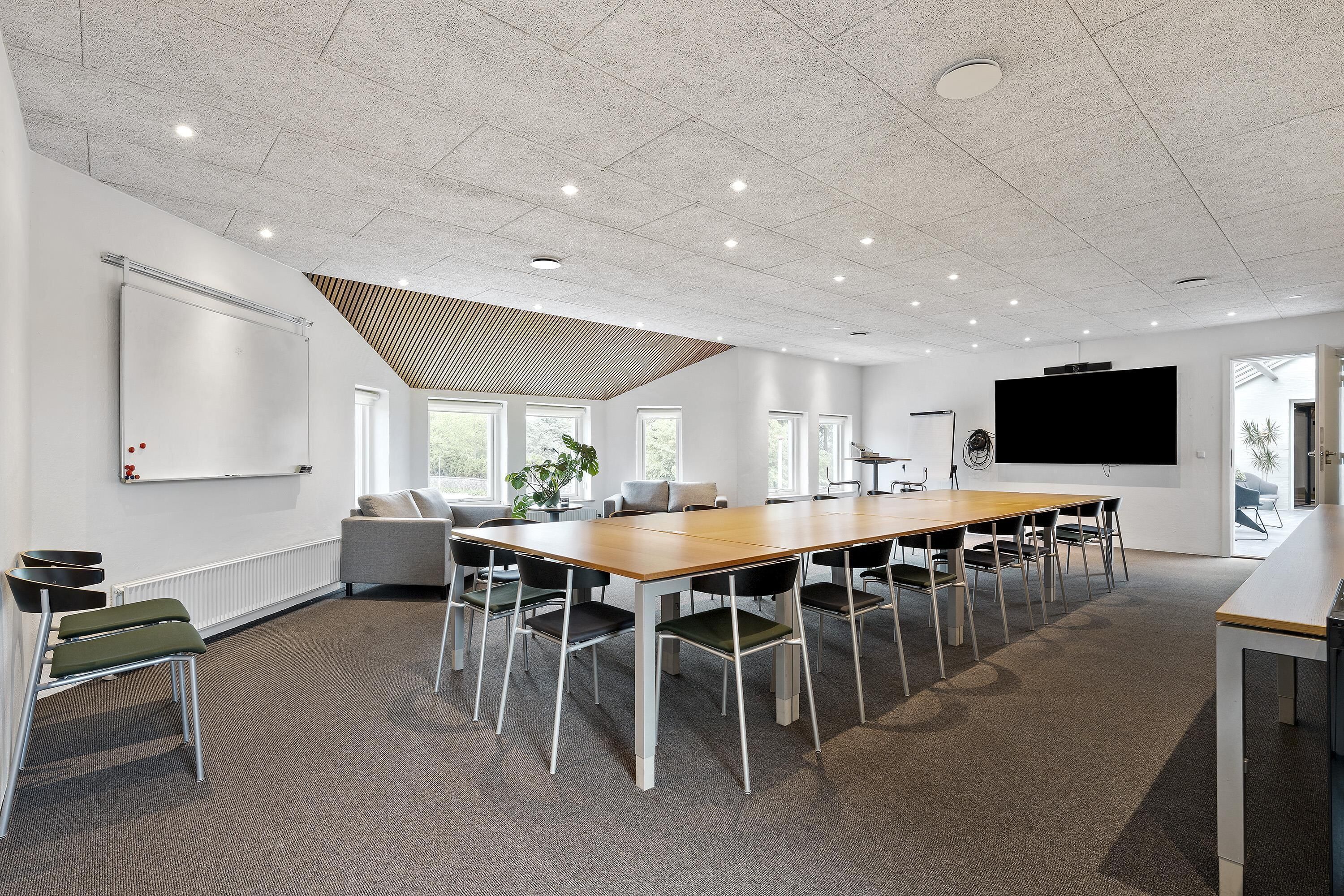 Een vergaderruimte met een lange tafel, stoelen, een whiteboard en een groot scherm.