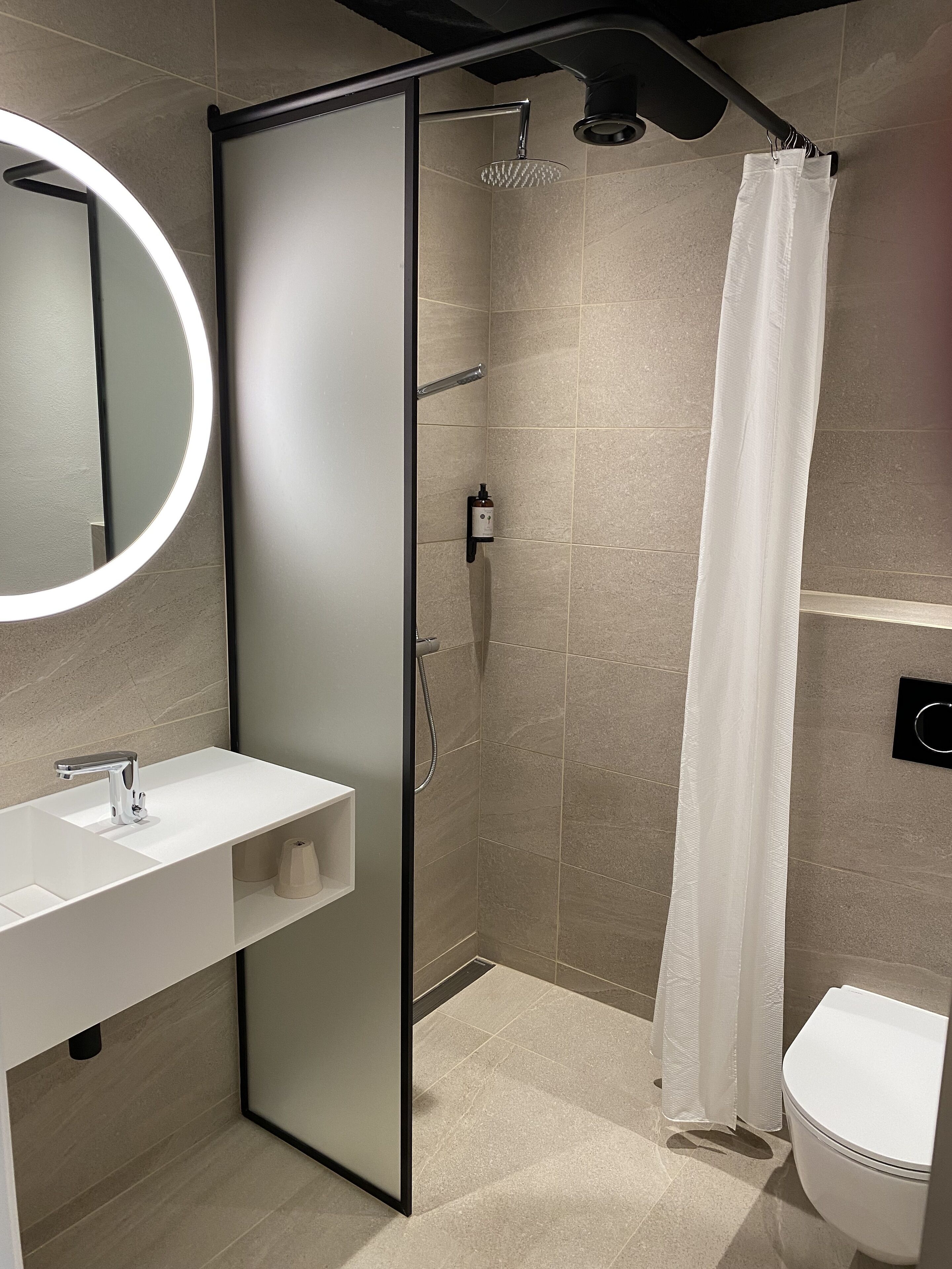 Et moderne badeværelse med en glasafskærmet brusekabine, en hvid vask og et toilet.