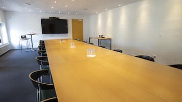 Uma sala de conferência com uma longa mesa de madeira, cadeiras, uma tela de TV e uma porta.