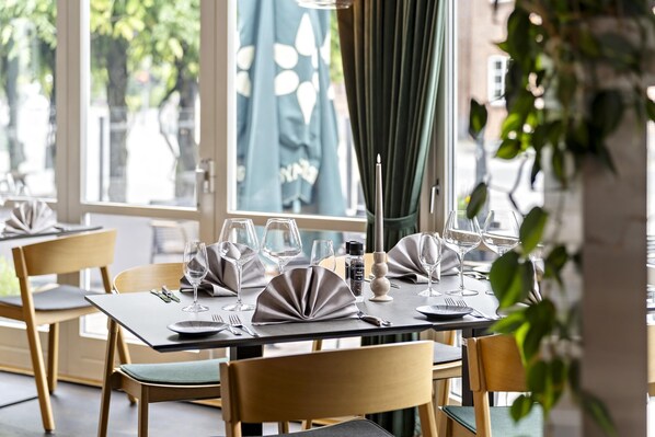 A dining area with tables set for a meal, chairs, and a large window with curtains.