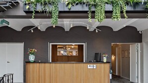 Una recepci ón con detalles de madera, un cartel que indica un baño y plantas colgantes en la parte superior.