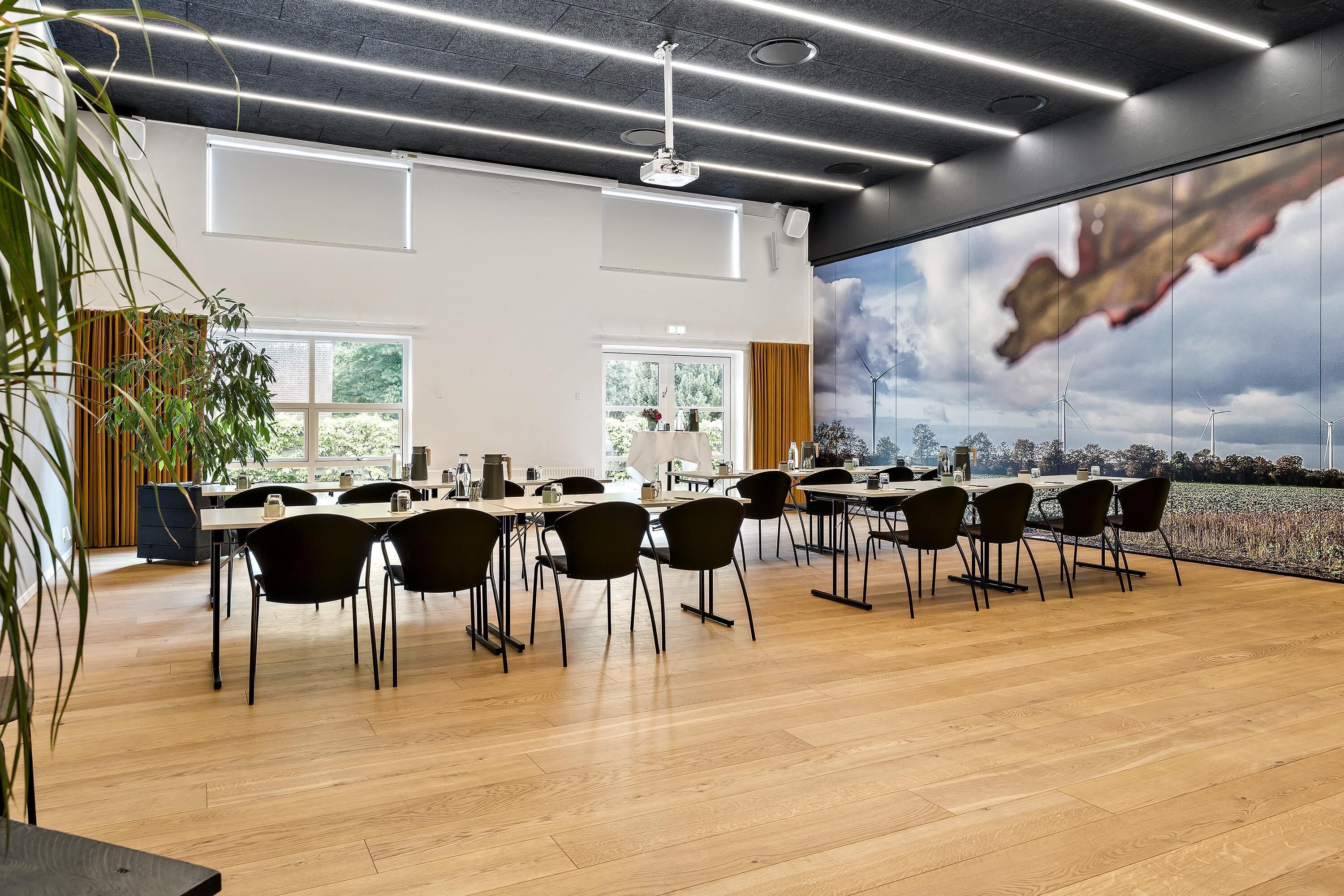 A modern conference room with a large table, chairs, and a view of wind turbines through a large window.