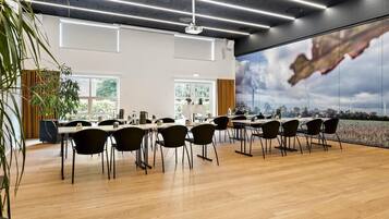 A modern conference room with a large table, chairs, and a view of wind turbines through a large window.