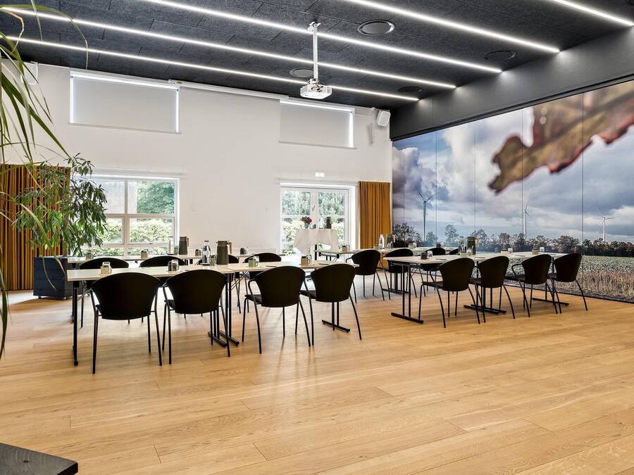 A modern conference room with a large table, chairs, and a view of wind turbines through a large window.