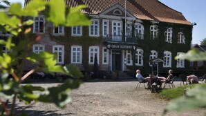 A building with a sign reading "GRAM SLOTSKRO" and a gravel courtyard with outdoor seating. - Gram Slotskro (Gram)