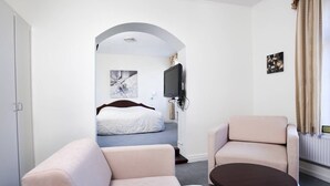 A hotel room with a sofa, a round table, a TV, and a bed with a white headboard. - Gram Slotskro (Gram)