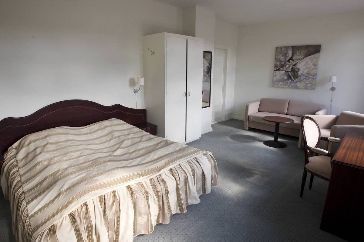 A hotel room with a large bed, a sofa, a small table, and a wardrobe.