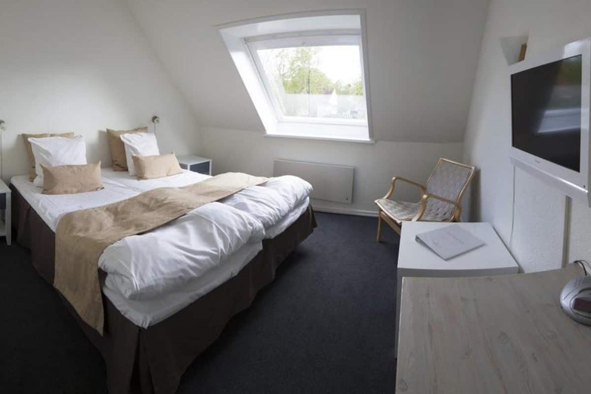 A bedroom with a bed, a chair, a desk, a television, and a window.