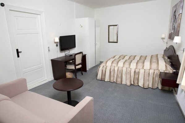 A hotel room with a bed, a desk with a chair, a television, a small table, and a sofa. - Gram Slotskro (Gram)