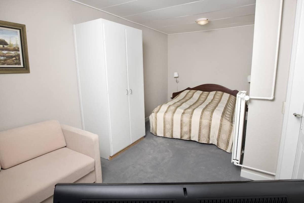 A bedroom with a bed, a white wardrobe, a beige sofa, and a painting on the wall.