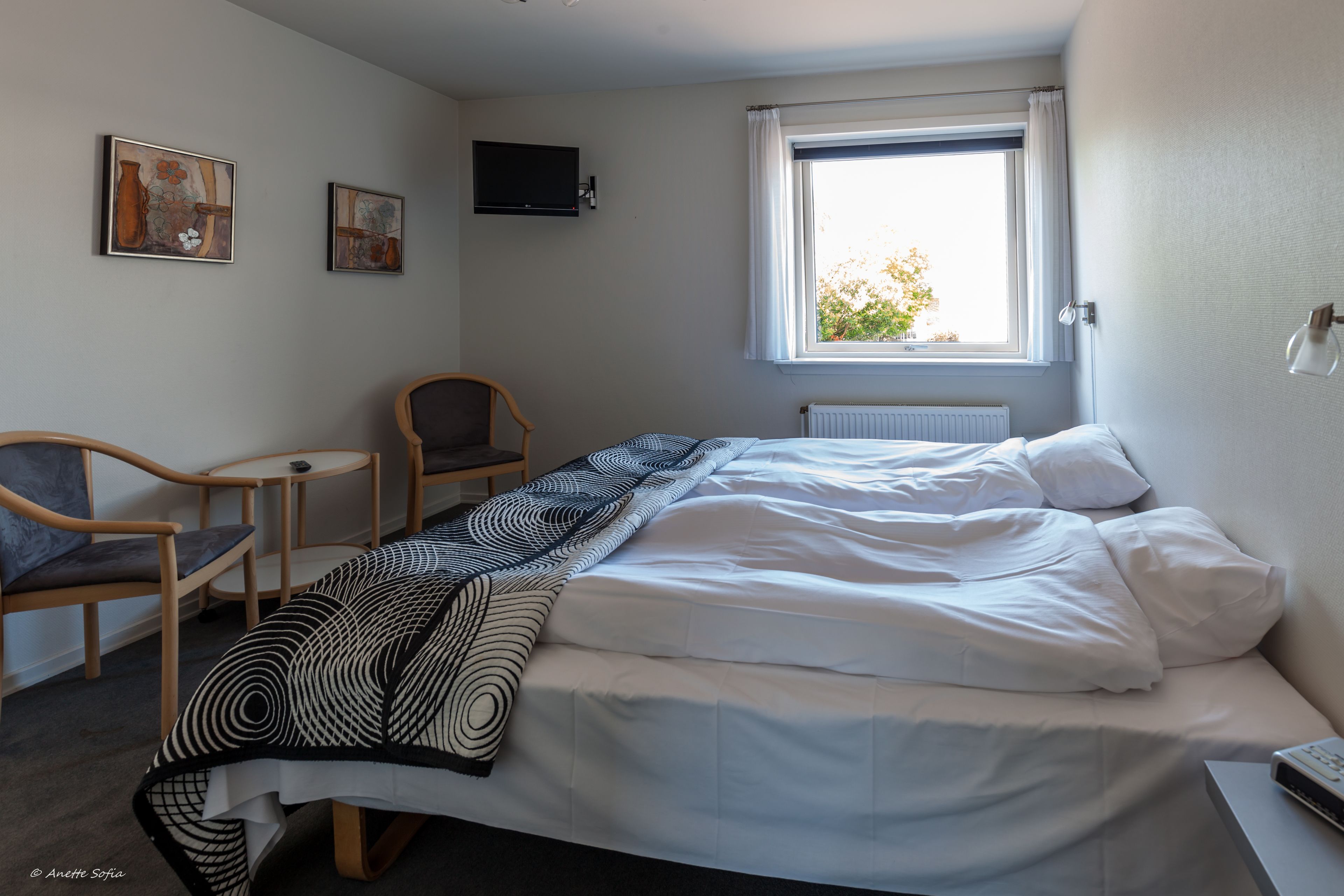 Un dormitorio con cama, una silla, una mesita y una ventana.