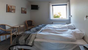 Un dormitorio con cama, una silla, una mesita y una ventana.