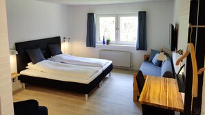 Una habitación con dos camas, un escritorio, una silla, un radiador, una ventana con cortinas y un televisor colgado en la pared.