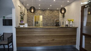 Un mostrador de recepción con detalles de madera, un fondo de pared de piedra y dos lámparas colgantes.