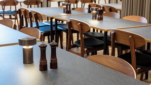 Een moderne eethoek met houten tafels en stoelen, een zout- en peperstel op de tafel, en een lamp.