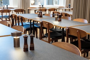 A modern dining area with wooden tables and chairs, a salt and pepper shaker on the table, and a lamp.
