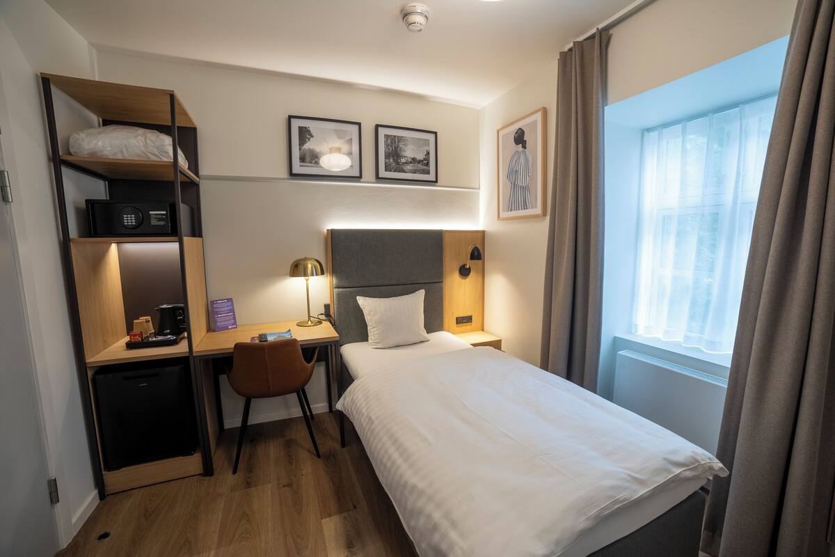 Habitación de hotel con cama, escritorio, silla y una pequeña kitchenette.