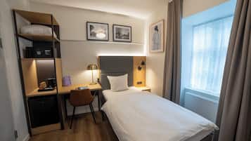 Et hotelværelse med seng, skrivebord, stol og et lille tekøkken.