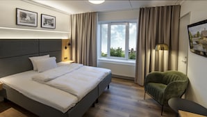 Een moderne hotelkamer met een groot bed, een groene fauteuil, een nachtkastje, een lamp en een raam met gordijnen.