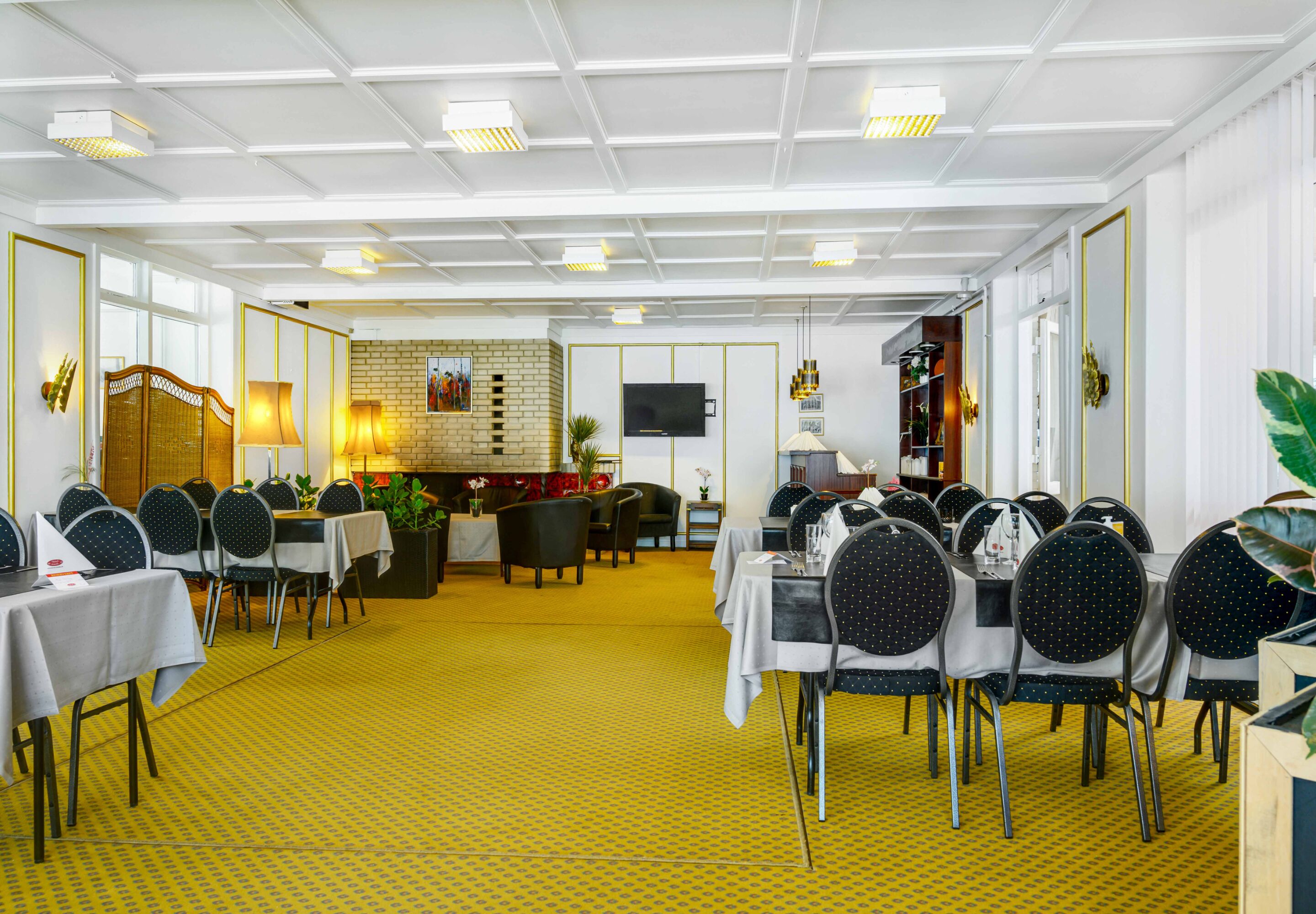 A spacious dining area with tables and chairs, a brick wall with a fireplace, and a television mounted on the wall.