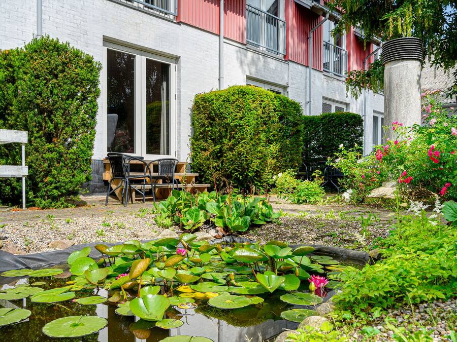 Un jardín con un estanque, plantas en macetas y una zona de estar con sillas y una mesa.