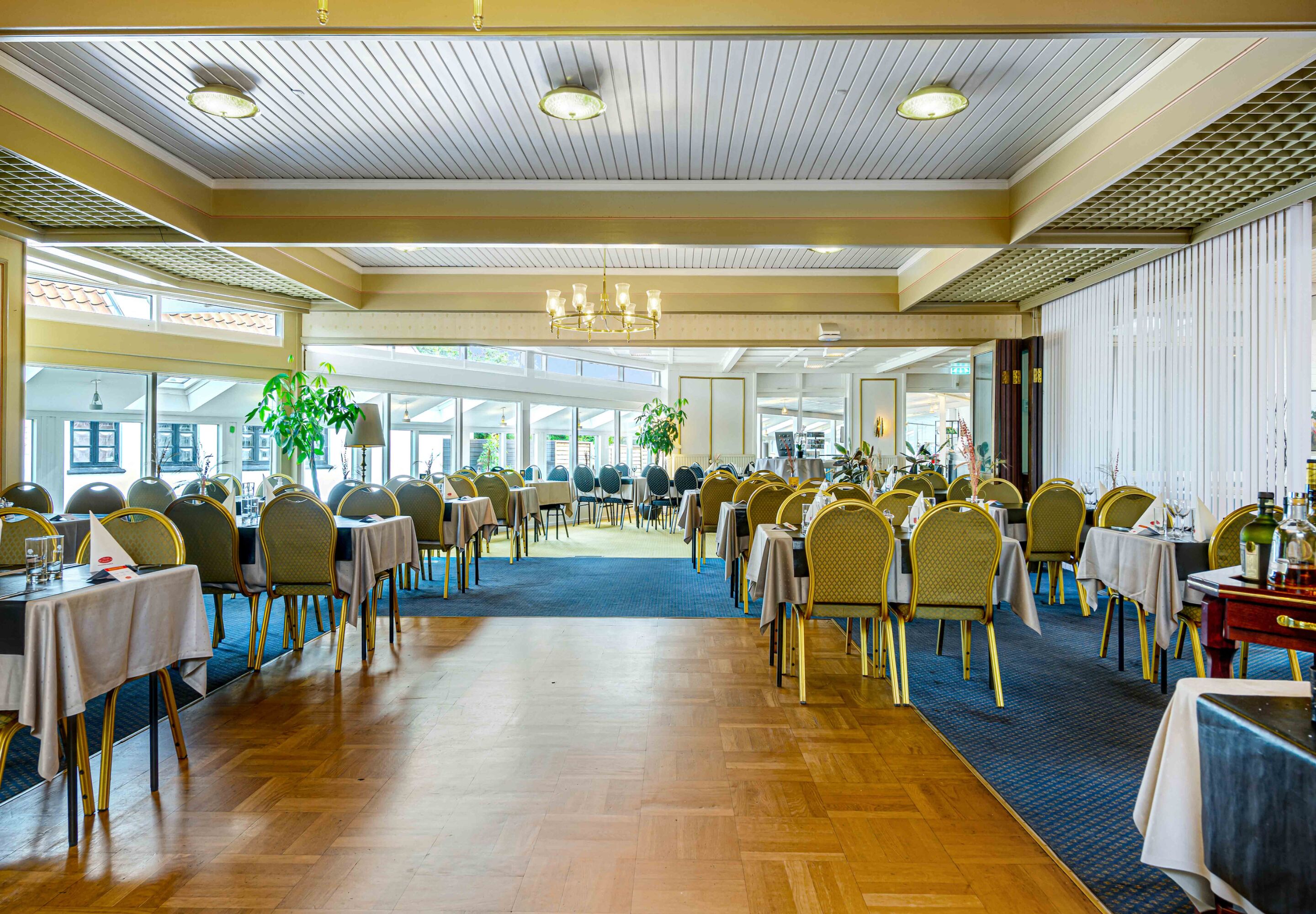 A spacious banquet hall with rows of tables and chairs, large windows, and a chandelier.