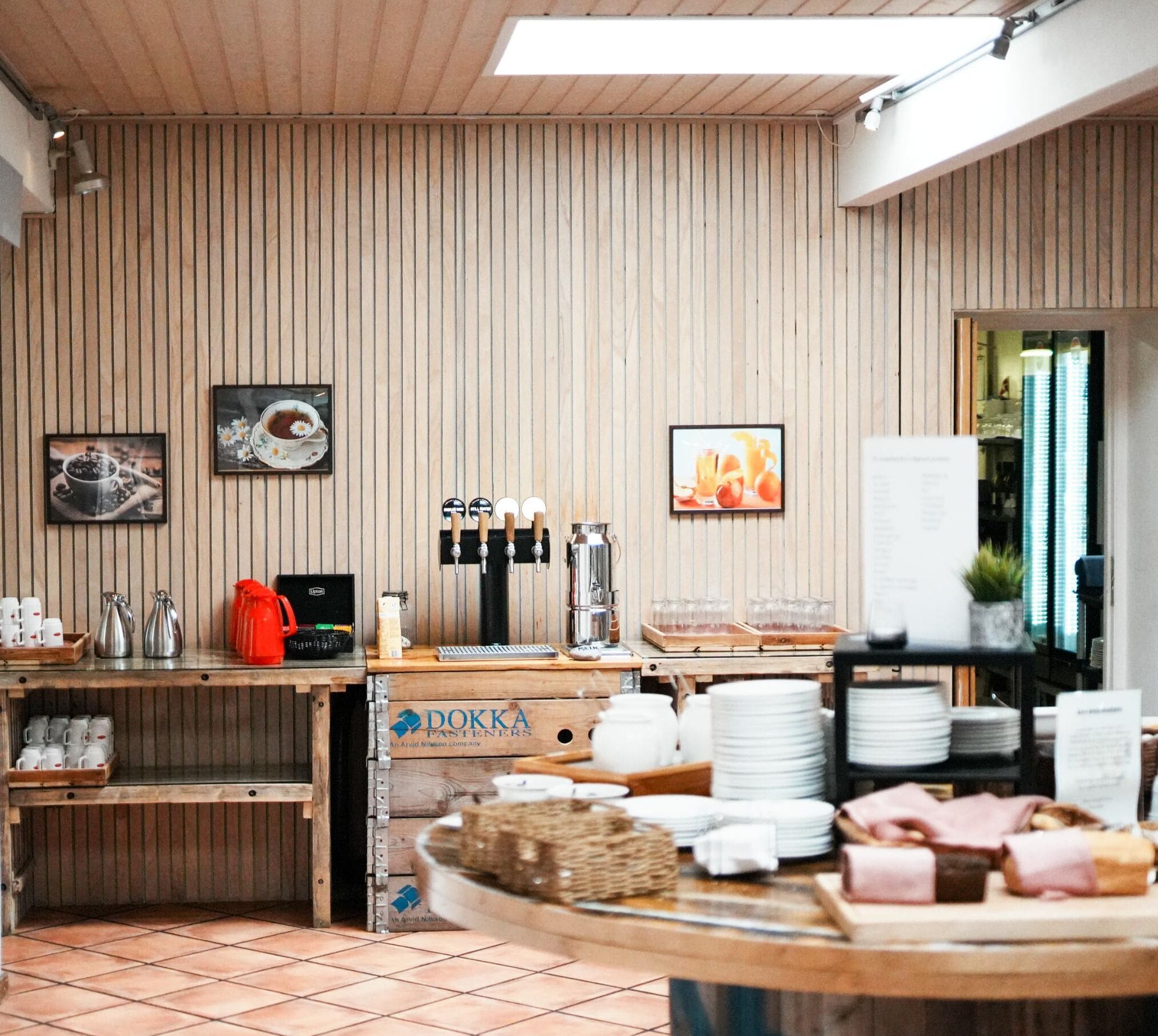 Una cafetería con paredes de paneles de madera, una estación de café y un bufé con platos y pan.