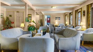 Un vestíbulo de hotel con techo alto, varias zonas de estar y una mesa central con una vela.