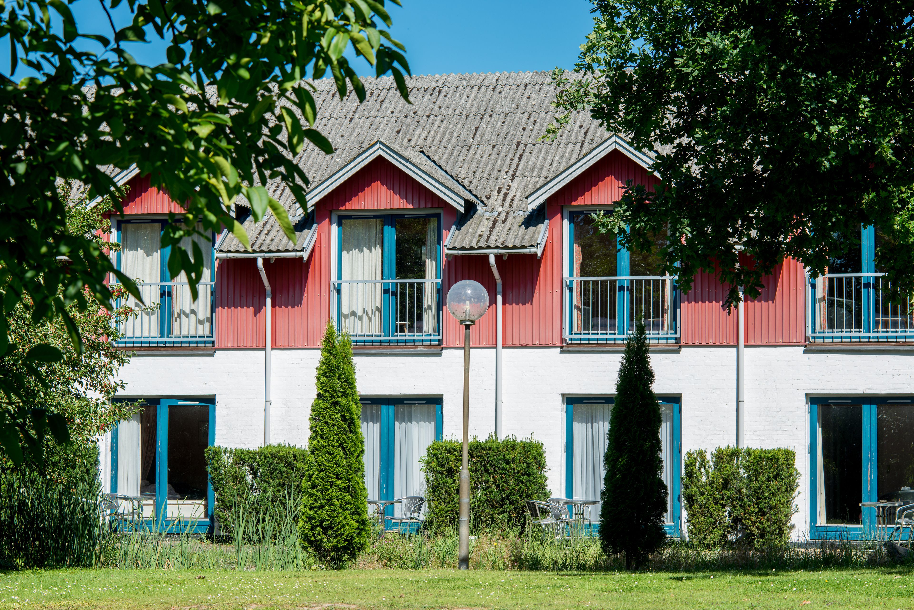 Un bâtiment rouge et blanc, doté de nombreuses fenêtres et de balcons, et entouré de verdure.