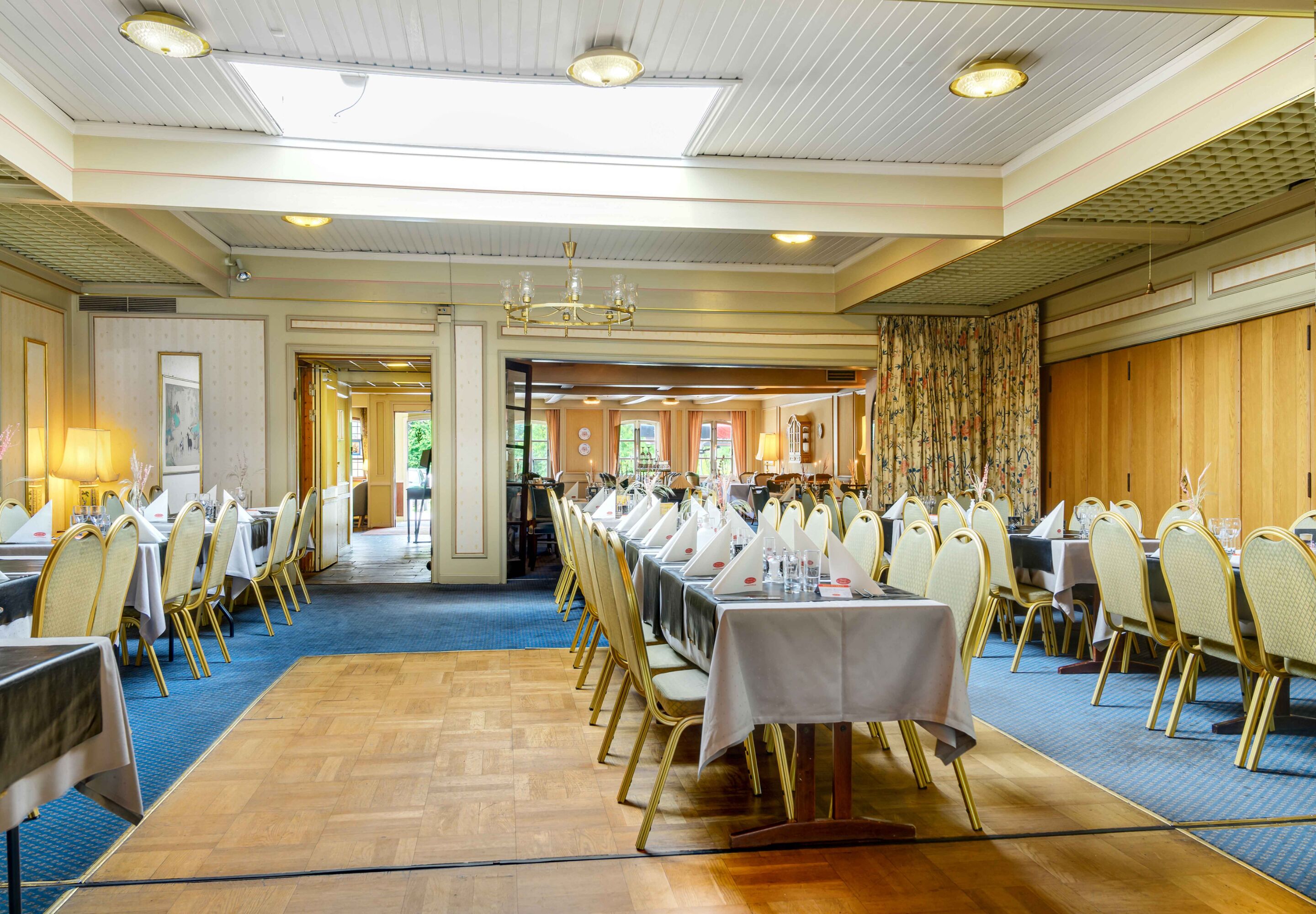 A banquet hall with long tables, chairs, and chandeliers.
