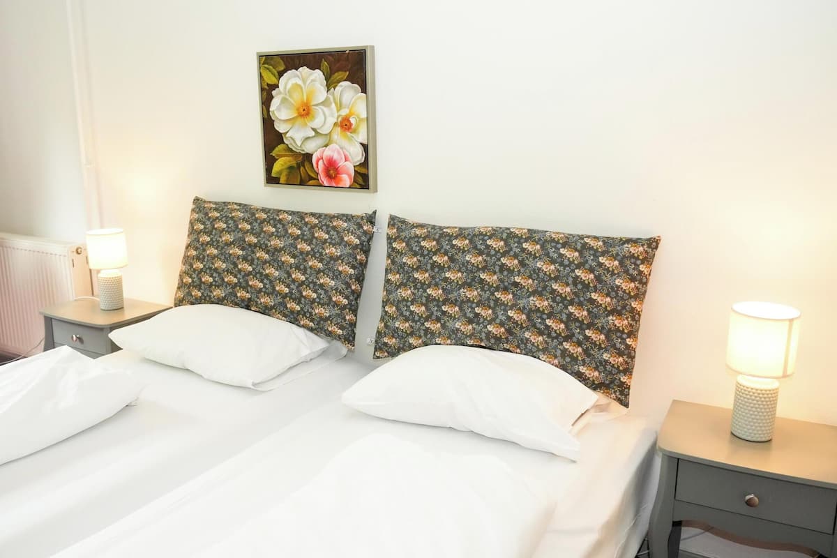 A double bed with white linens, two matching floral-patterned pillows, and two bedside tables with lamps.