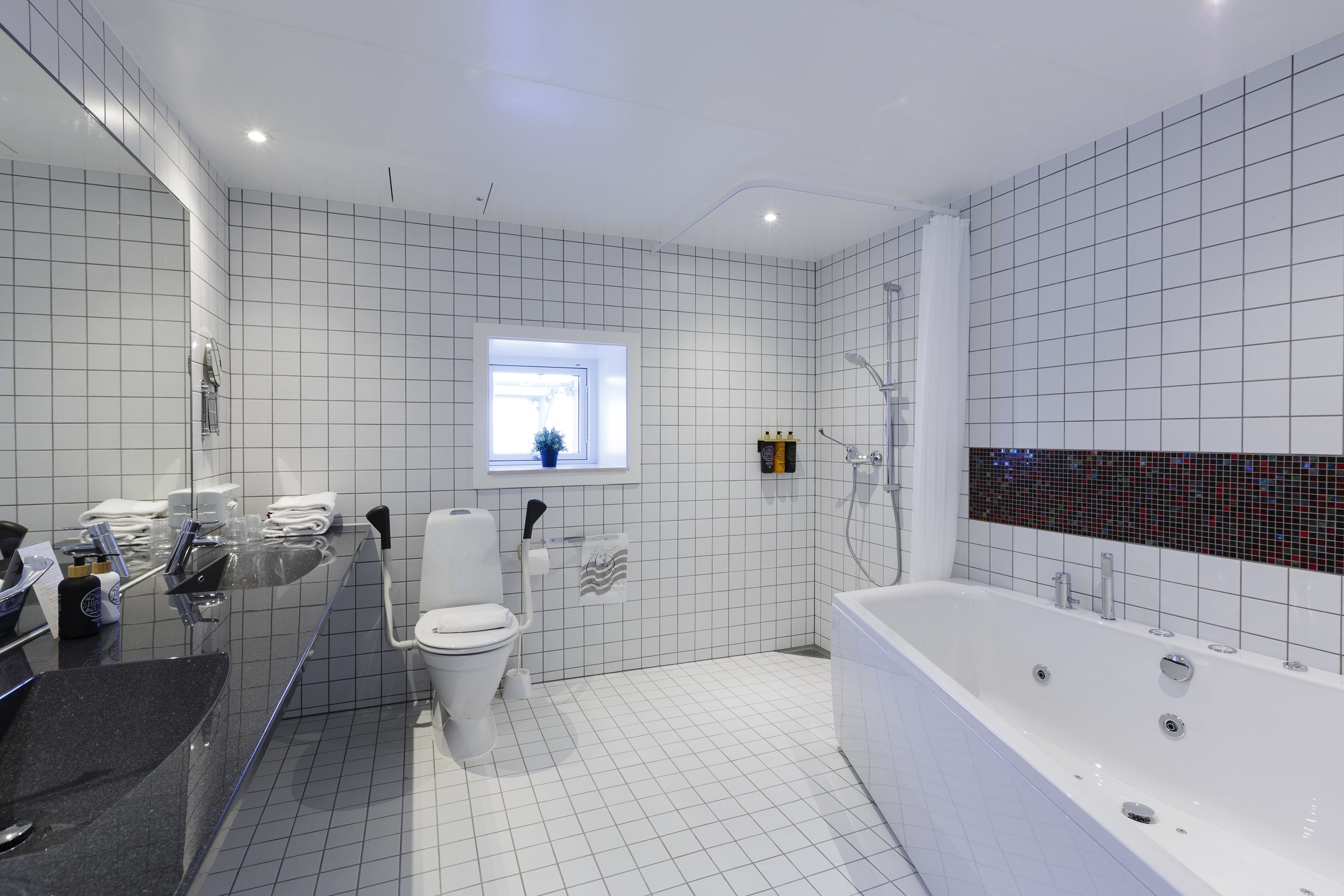 Un baño moderno con lavamanos de superficie negra, inodoro blanco y una bañera blanca grande.